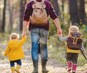 A dad walking with his two children on a woodland trail